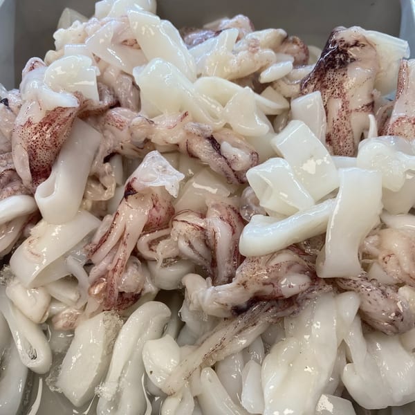 Freshly prepared squid, both rings and tentacles, with some dark markings, ready for cooking.