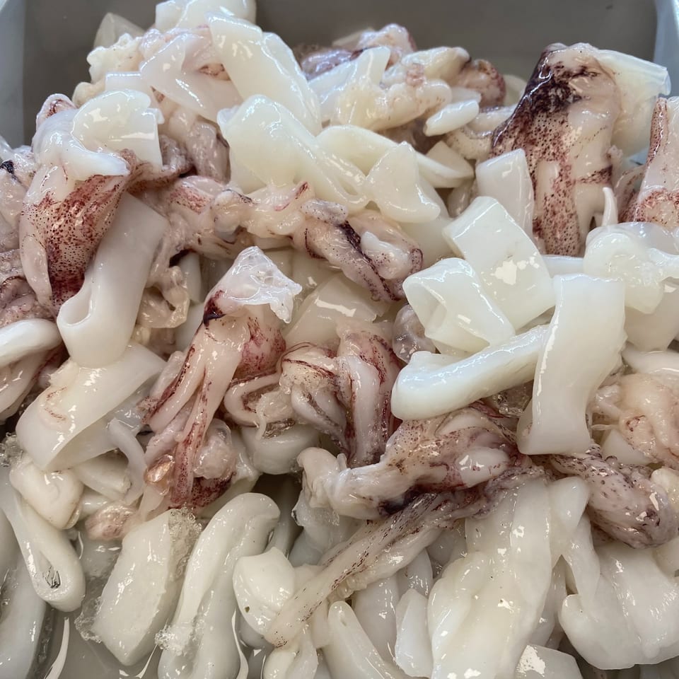 Freshly prepared squid, both rings and tentacles, with some dark markings, ready for cooking.