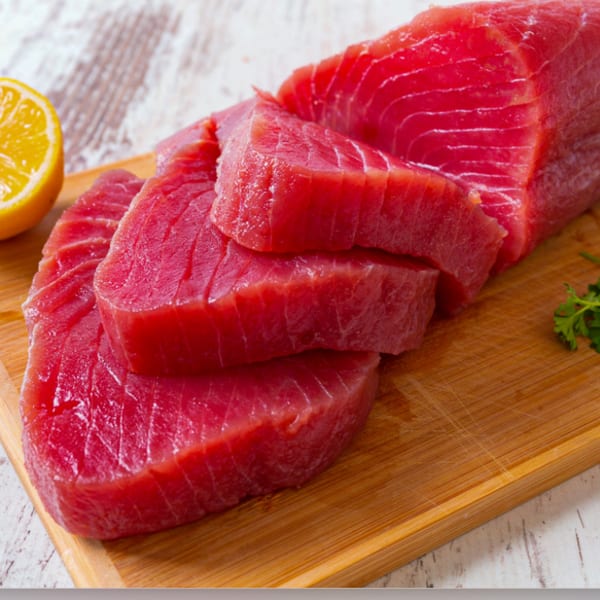 Fresh, vibrant red tuna steaks and slices on a wooden cutting board with a lemon half.