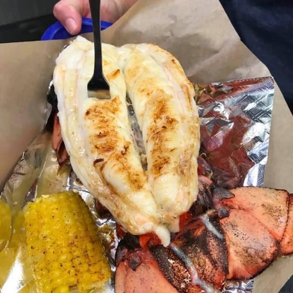 Grilled lobster tail and claws with corn on the cob, served in foil and paper.