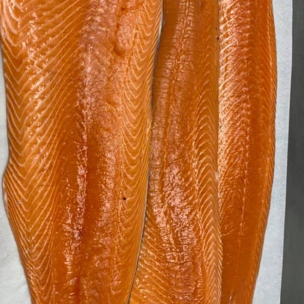 Three vibrant orange salmon fillets with distinct muscle lines are arranged on a white surface.